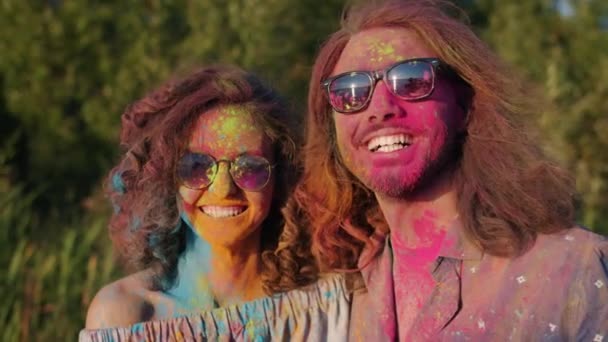 Μικτή φυλή ζευγάρι με πολύχρωμα πρόσωπα και τα μαλλιά χαμογελώντας κατά τη διάρκεια Holi φεστιβάλ διασκεδάζοντας σε εξωτερικούς χώρους — Αρχείο Βίντεο