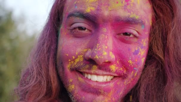 Close-up portrait of attractive Middle Eastern guy student covered with gulal paint standing outdoors — Stock Video