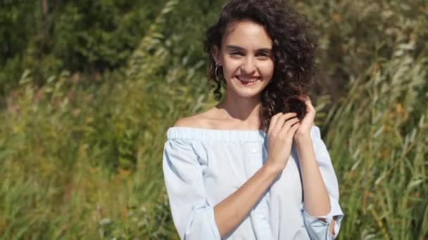 Lassú mozgás portré vidám fiatal hölgy áll a szabadban a szeles és napos nyári nap mosolygós — Stock videók