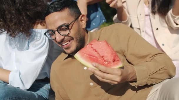 Медленный портрет счастливого араба, смеющегося и поедающего арбуз на пикнике с друзьями — стоковое видео