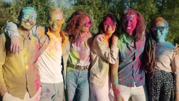 Portré boldog barátok színes arcok haj és ruhák áll a szabadban, és mosolyog a Holi fesztivál — Stock videók