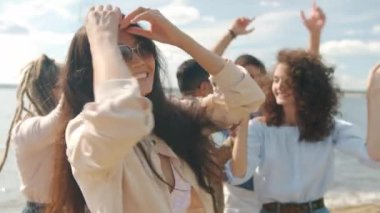 Sahilde dans eden neşeli Asyalı kadın yaz günü çok ırklı arkadaşlarıyla eğleniyor.