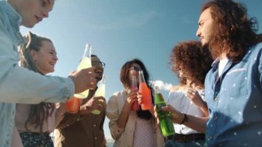 Yavaş çekimde neşeli arkadaşların şişeleri tokuşturup, içip sahilde eğlenen portresi.