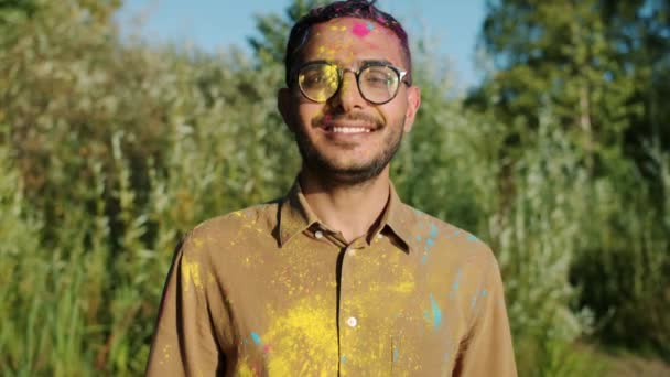 Retrato del gracioso hombre de Oriente Medio divirtiéndose en el festival Holi mientras sus amigos le tiran pintura — Vídeo de stock