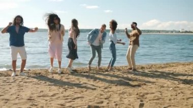 Mutlu arkadaşlar çok ırklı gruplar dans ederek zıplıyorlar güzel kumsalda gülüyorlar