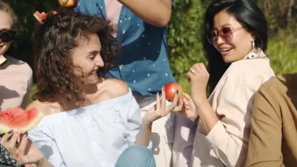 Vreugdevolle jonge vrouw praten met vrienden dansen en eten watermeloen op picknick buiten — Stockvideo