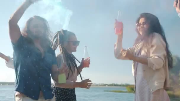Zpomalený pohyb veselých dívek a chlapů tančících s kouřovými bombami na pláži a popíjejících z lahví — Stock video