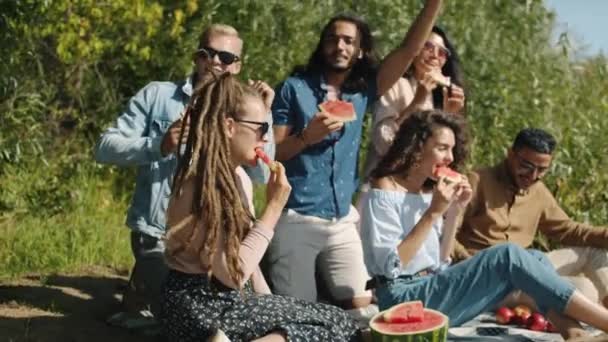 Fröhliche Freunde Multi-ethnische Gruppe essen Wassermelone reden und tanzen im Freien im Park — Stockvideo