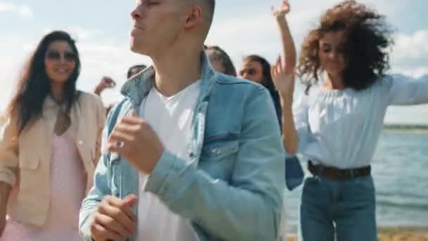 Portrait au ralenti de mecs blonds joyeux dansant sur la plage avec des amis souriants profitant de l'heure d'été — Video