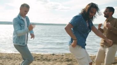 Çok ırklı bir grup erkek sahilde dans ediyor. Yaz günü şarkı söylüyorlar.