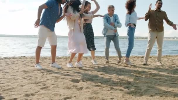 Movimiento lento de los millennials creativos saltando y bailando en la playa divirtiéndose juntos — Vídeos de Stock