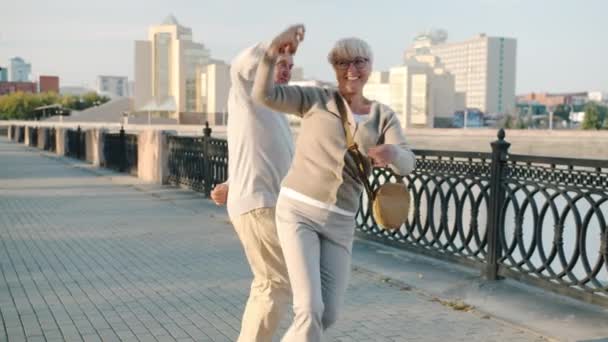 Homem e mulher sênior feliz dançando na rua da cidade sorrindo desfrutando de relacionamento romântico no dia de verão — Vídeo de Stock