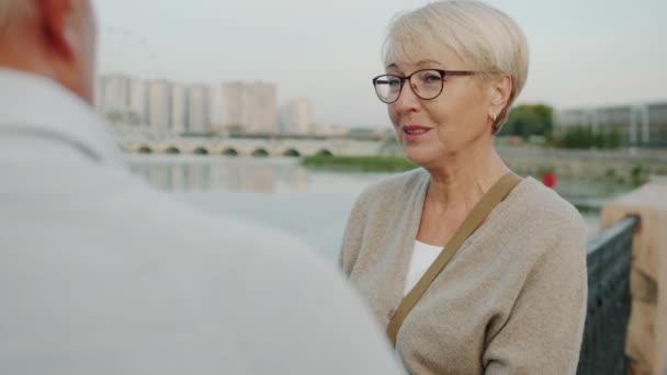 Gammal kvinna pratar med äldre man står utomhus och titta på flod och stad landskap på sommaren morgon — Stockvideo