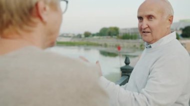 Mutlu kıdemli adam yaz sabahı şehir manzarası ve nehri seyreden bir kadınla konuşuyor.