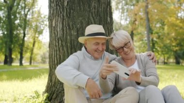 Akıllı telefon kullanan ve parkta içeriği tartışan neşeli çiftlerin yavaş çekimde portresi.