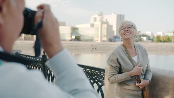 Радостная зрелая леди позирует для камеры, развлекаясь с рекой и красивым городом на заднем плане — стоковое видео
