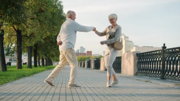 Joyful bejaarde paar dansen buiten plezier in de rivier dijk genieten van de zomerochtend in de stad — Stockvideo