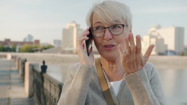 Alegre anciana chateando en el teléfono móvil sonriendo de pie en la ciudad moderna solo — Vídeo de stock