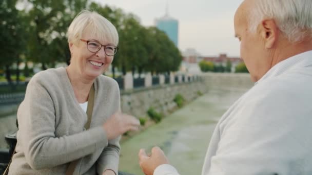 Pareja feliz hombre y mujer hablando y haciendo gestos riendo de pie en el terraplén del río en la ciudad — Vídeos de Stock