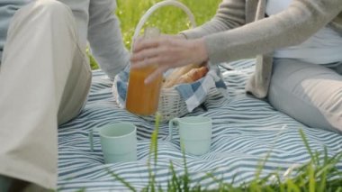 Yaz günü parkta piknik yaparken yaşlı kadınların ellerinin bardaklara meyve suyu doldurduğu yakın plan.