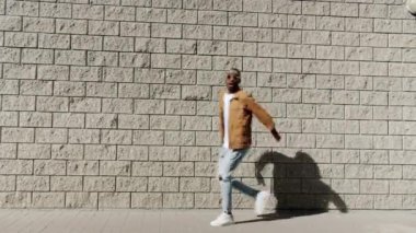 Neşeli Afro-Amerikalı bir adam sokakta yürüyor sonra zıplıyor ve dışarıda gülüyor.