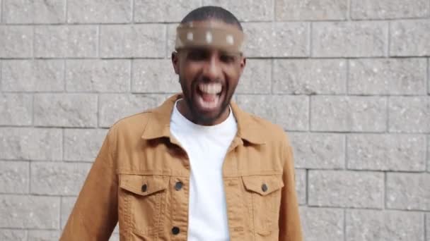 Retrato de estudante afro-americano alegre acenando cabeça e rindo ao ar livre contra fundo da parede — Vídeo de Stock