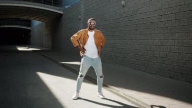 Neşeli Afro-Amerikalı adam dans ediyor ve arka planda modern binalarla dışarıda eğleniyor.