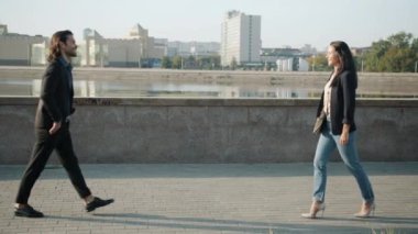 Neşeli genç adam ve kadın nehir kenarında yürüyorlar ve gülümsüyorlar.