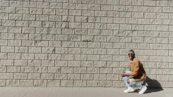 Zabawny młody Afroamerykanin spacerujący po swoich przystojniakach śmiejący się z cegły pod ścianą — Wideo stockowe