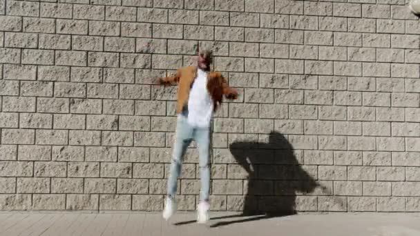 Bucle sin fin de feliz hombre afroamericano saltando al aire libre contra el fondo de la pared de ladrillo — Vídeo de stock