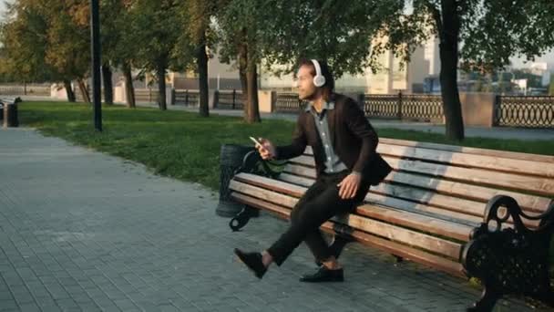 Looping av stilig affärsman koppla av utomhus lyssna på musik med smartphone och hörlurar — Stockvideo