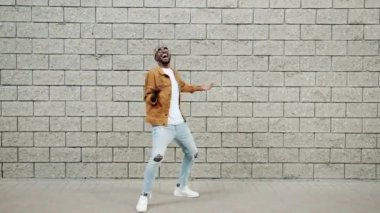 Kaygısız Afro-Amerikalı adamın portresi beyaz duvar arkasında modern hareketler yapıyor.