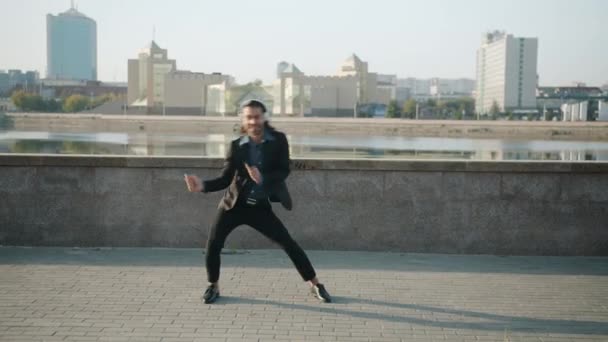 Boucle de jeune homme d'affaires heureux portant des écouteurs dansant en plein air dans le remblai de la rivière — Video