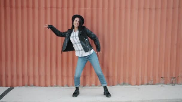 Dance loop aranyos lány hipster, hogy hullám mozog a karok mosolygó pihentető a falon háttér — Stock videók