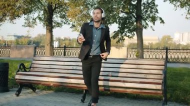 Şehirde bankta oturan, kulaklık takan ve akıllı telefon kullanan neşeli melez iş adamlarının döngüsü.