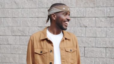 Mutlu Afro-Amerikalı bir adamın portresi. Kafa dansı yapıyor. Açık havada kameraya bakıp gülümsüyor.