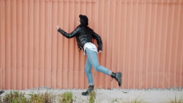 Цикл современной девушки в стильной одежде, танцующей на открытом воздухе на фоне стен — стоковое видео