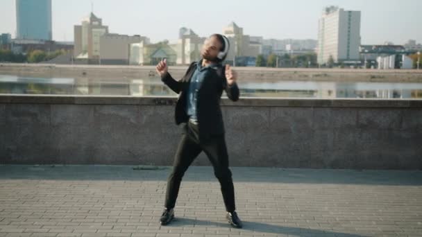 Retrato de guapo morena bailando y aplaudiendo con auriculares al aire libre en la ciudad — Vídeos de Stock