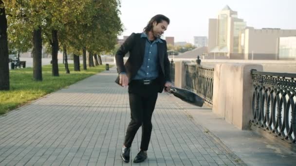 Langzame beweging van gelukkige man in pak dansen en gooien aktetas genieten van de dag buiten — Stockvideo