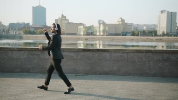 Looping de hombre de negocios feliz caminando al aire libre saltando con auriculares — Vídeos de Stock