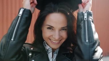 Yakın çekim yavaş çekimde genç bir kadının modayı takip eden şapkasını takıp kameraya bakarken gülümsemesi.