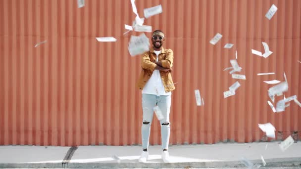 Hombre afro-americano confiado lanzando dinero en efectivo y luego parado al aire libre con los brazos cruzados y mirando a la cámara — Vídeos de Stock