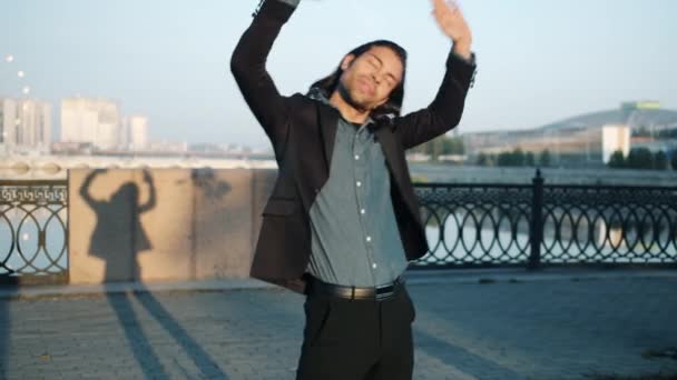 Cool chico de raza mixta bailando al aire libre en el terraplén del río divirtiéndose moviéndose sobre fondo urbano — Vídeos de Stock