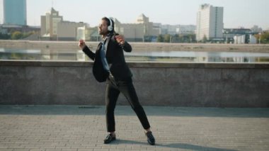 Kulaklıklı, dans eden ve el çırpan mutlu genç adamın ağır çekimde portresi.