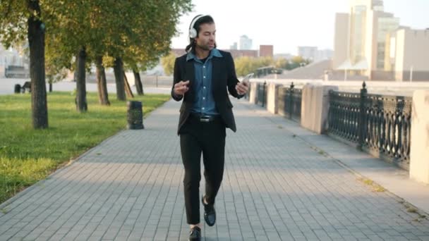 Glada affärsman promenader i staden bär hörlurar med smartphone dans ha kul — Stockvideo