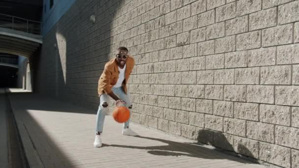Радостный афро-американский спортсмен веселится с баскетболом, играя в одиночку на улице города — стоковое видео