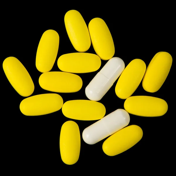 Желтые таблетки и белые капсулы на чёрном фоне — стоковое фото