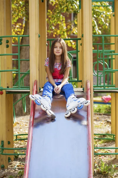 Niña sentada en el patio de recreo en patines — Foto de Stock