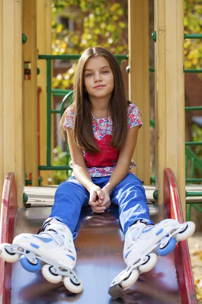 Menina sentada no parque infantil em patins — Fotografia de Stock