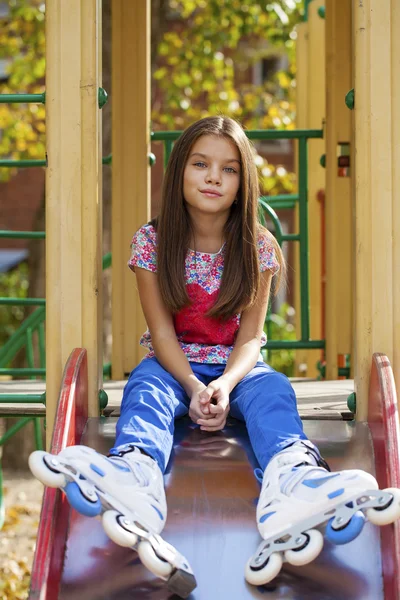 Niña sentada en el patio de recreo en patines — Foto de Stock